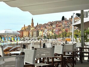 A terrace with outdoor seating overlooking a coastal cityscape with historic buildings. - Beautiful 3 pieces in luxury residence 50 meters from the sea (Menton)