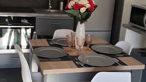 A modern kitchen with grey cabinets, a stainless steel refrigerator, and a dining table set for four with white chairs. - Beautiful 3 pieces in luxury residence 50 meters from the sea (Menton)