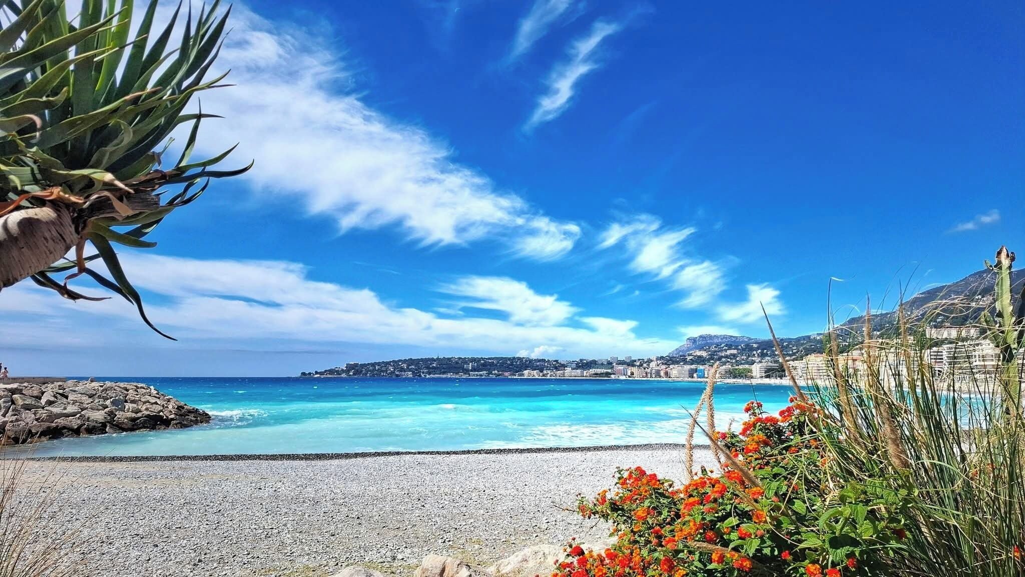 Une vue sur la côte, avec un ciel dégagé, une plage de galets et une ville située au loin.