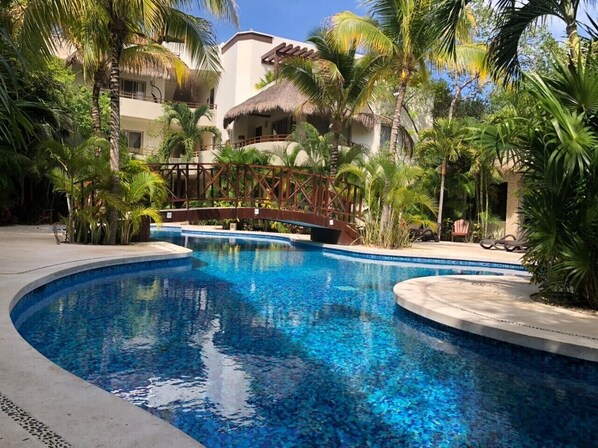 A swimming pool surrounded by palm trees and a building with a thatched roof.