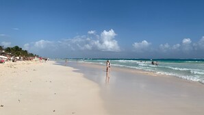 A wide sandy beach with gentle waves, palm trees, and a clear sky.