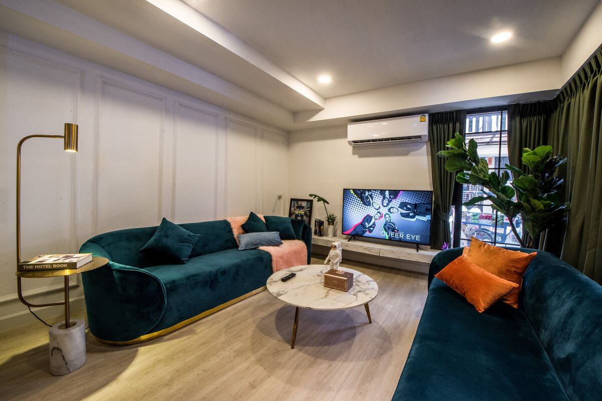 Un saló modern amb un sofà color esmeralda, una taula de centre de marbre i un televisor que mostra un programa.