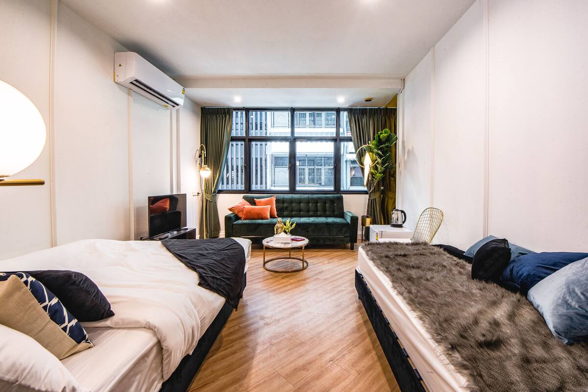 Habitació d'hotel moderna amb dos llits, un sofà, una televisió i un gran finestral amb cortines.