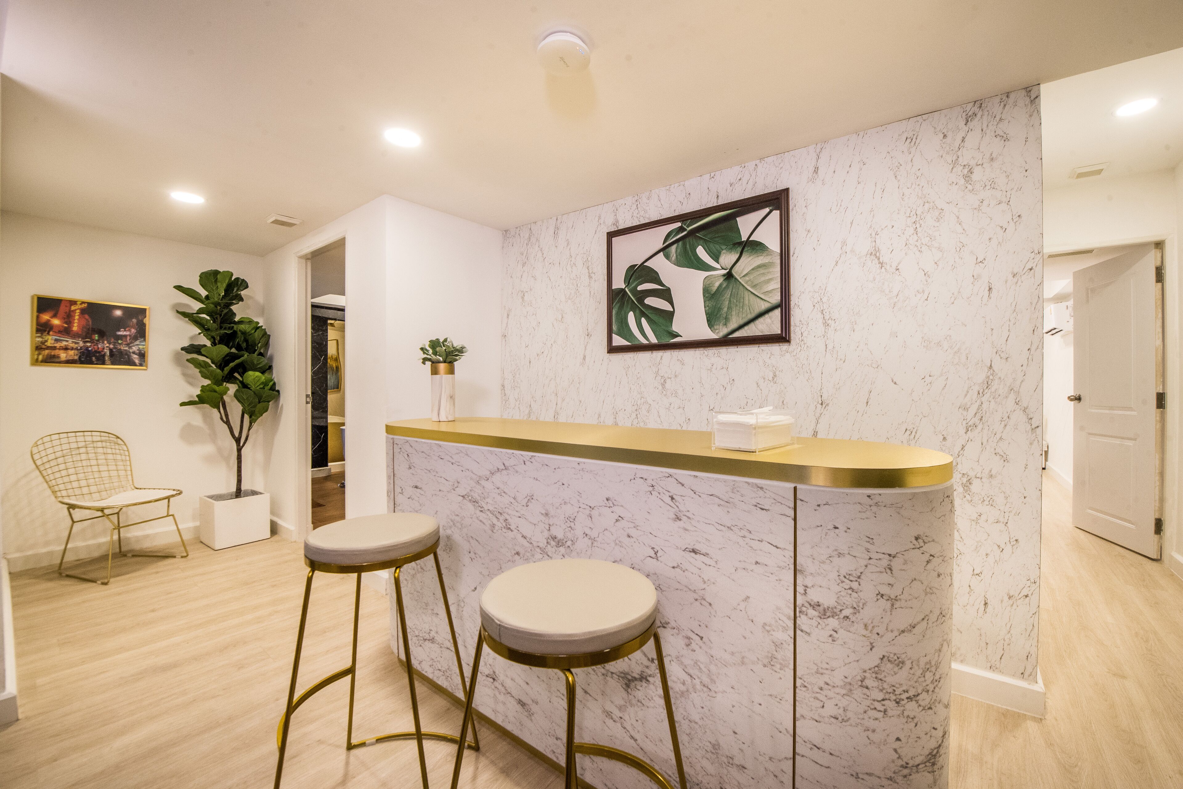 Une cuisine moderne avec un plan de travail en marbre, deux tabourets, une plante en pot et un tableau encadré au mur.