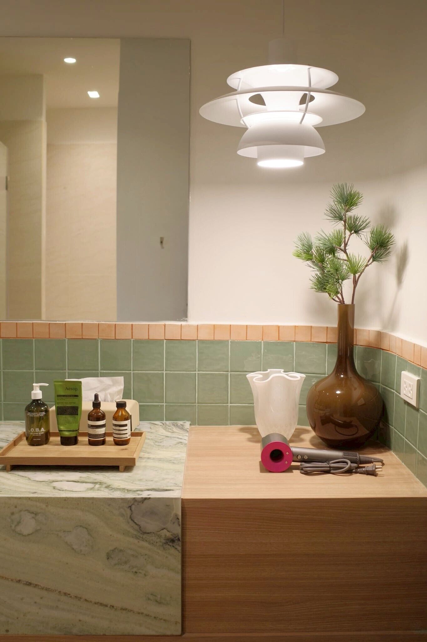 A bathroom with a wooden vanity, a mirror, a vase with a plant, and toiletries on a tray.