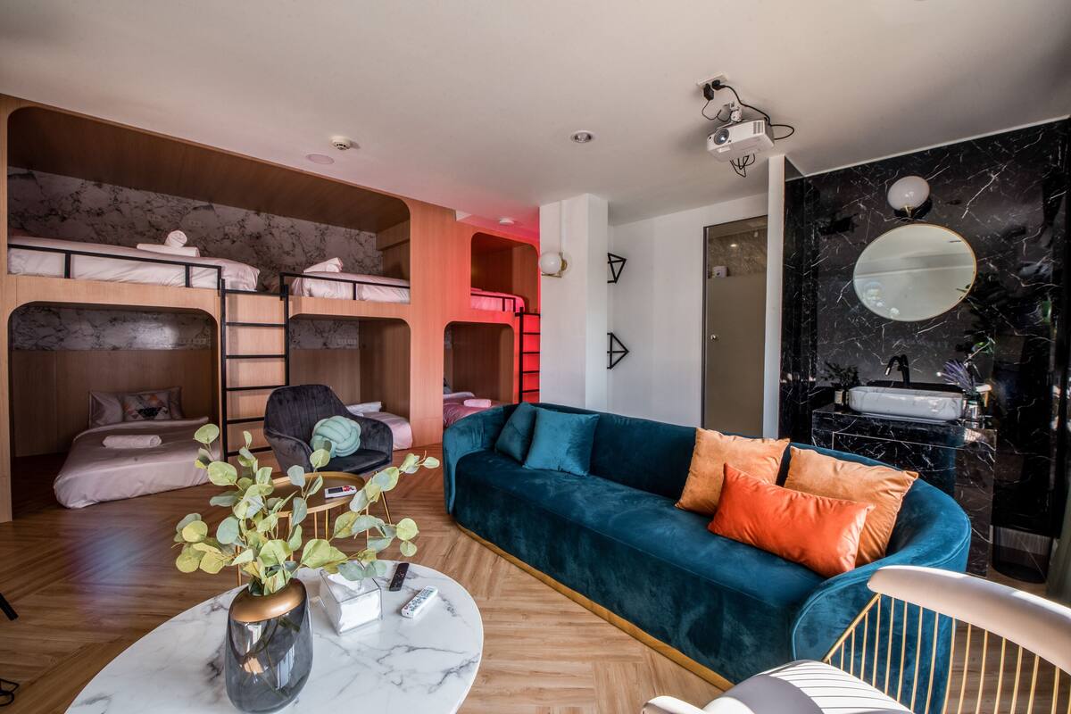 Habitació moderna amb llits superposats, un sofà blau, una taula de cafè de marbre i un bany amb paret de marbre negre i un mirall rodó.