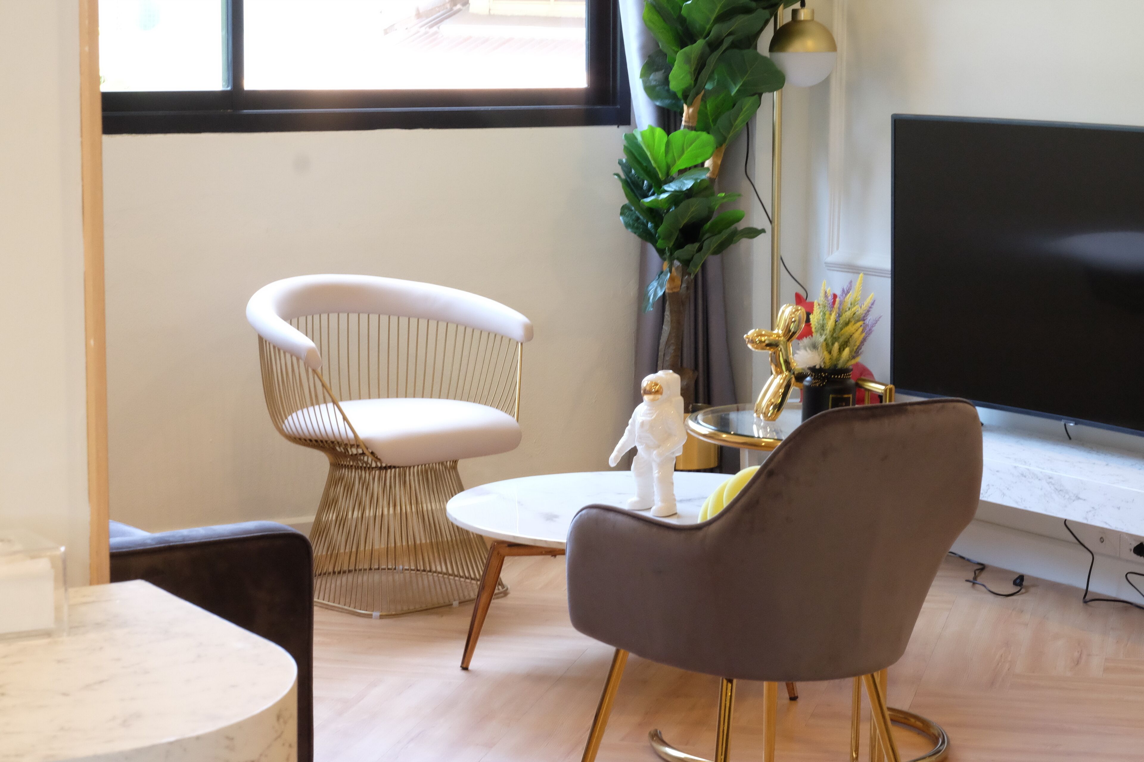 Een moderne woonkamer met een grote flatscreen televisie, een ronde salontafel, een witte gestoffeerde fauteuil, een donkere armstoel en een decoratieve plant.