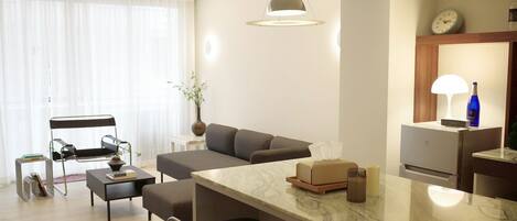 A modern living room with a sofa, a dining area with a marble countertop, a lamp, and a clock on the wall.
