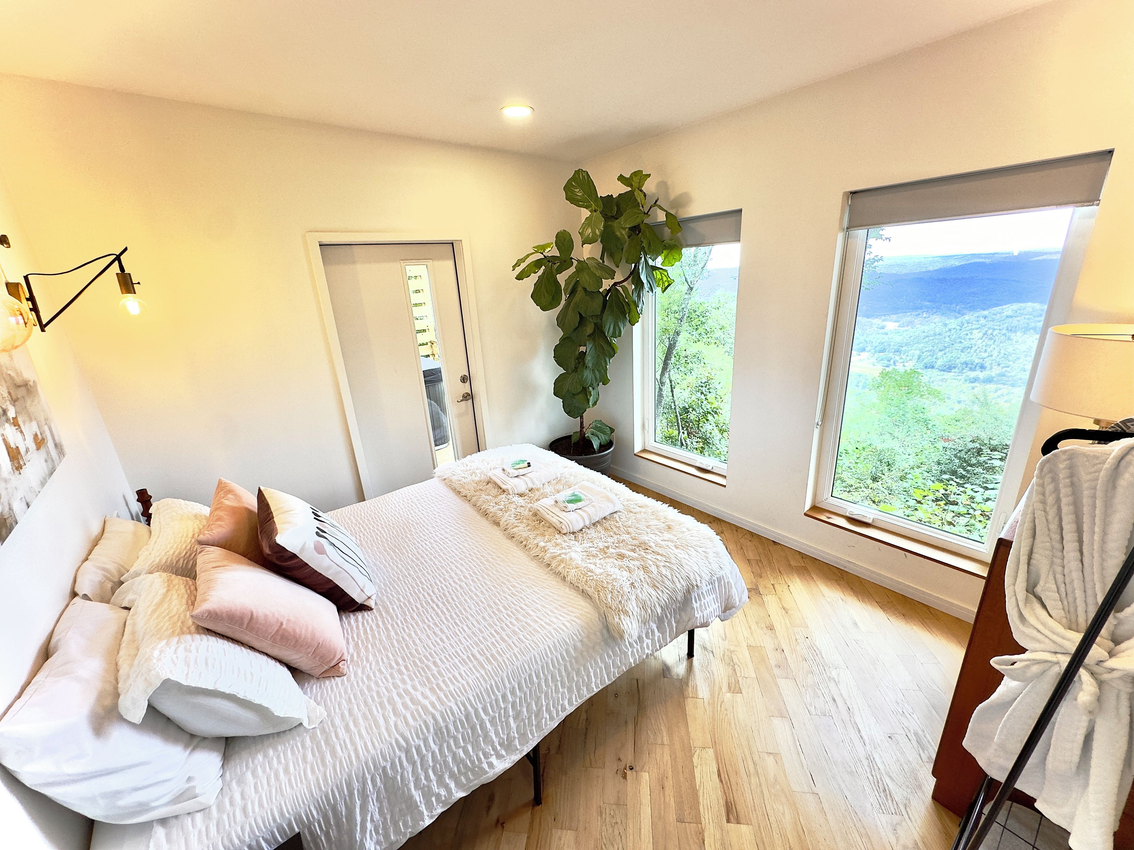 A bedroom with a bed, a potted plant, and a view of the outdoors.
