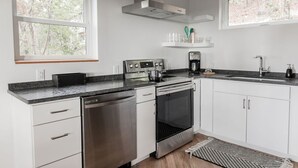 Una cucina moderna con mobili bianchi, elettrodomestici in acciaio inossidabile, un lavello doppio e una finestra con vista sul verde.