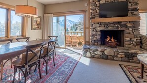Un salón acogedor con chimenea de piedra, una zona de comedor con mobiliario de madera y un ventanal con vistas a un paisaje montañoso.