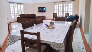 A spacious dining area with a long table, chairs, and a television mounted on the wall. - House in Ubatuba - Gated community | swimming pool | gourmet area | river access (Horto (Morro das Moças))