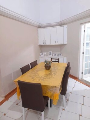 A dining area with a yellow table, six chairs, a cabinet above, and a tiled floor.