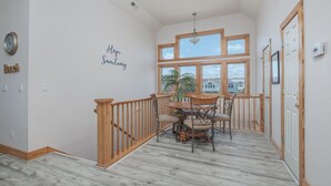 A dining area with a wooden table and chairs, a potted plant, and a view through large windows. - 1414 - Hope Sanctuary - Whalehead Corolla Escape | Pool, HotTub & Foosball (Corolla)