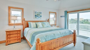 A bedroom with a wooden bed, a nightstand with drawers, a ceiling fan, and a large window with a view of the outdoors. - 1414 - Hope Sanctuary - Whalehead Corolla Escape | Pool, HotTub & Foosball (Corolla)