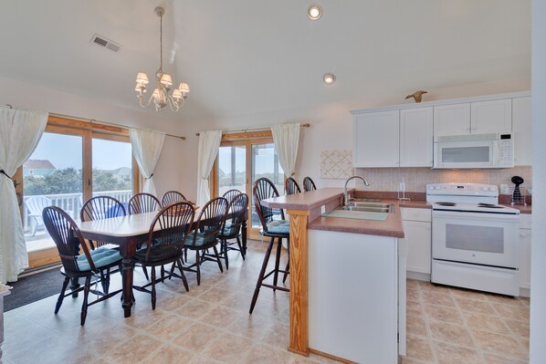 Una cocina moderna con armarios blancos, microondas integrado y estufa. Hay una zona de comedor con una mesa y sillas de madera.