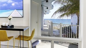 A room with a view of a beach, a table with chairs, and a TV mounted on the wall. - Ocean Treasure Beachside Suites (Lauderdale-by-the-Sea)