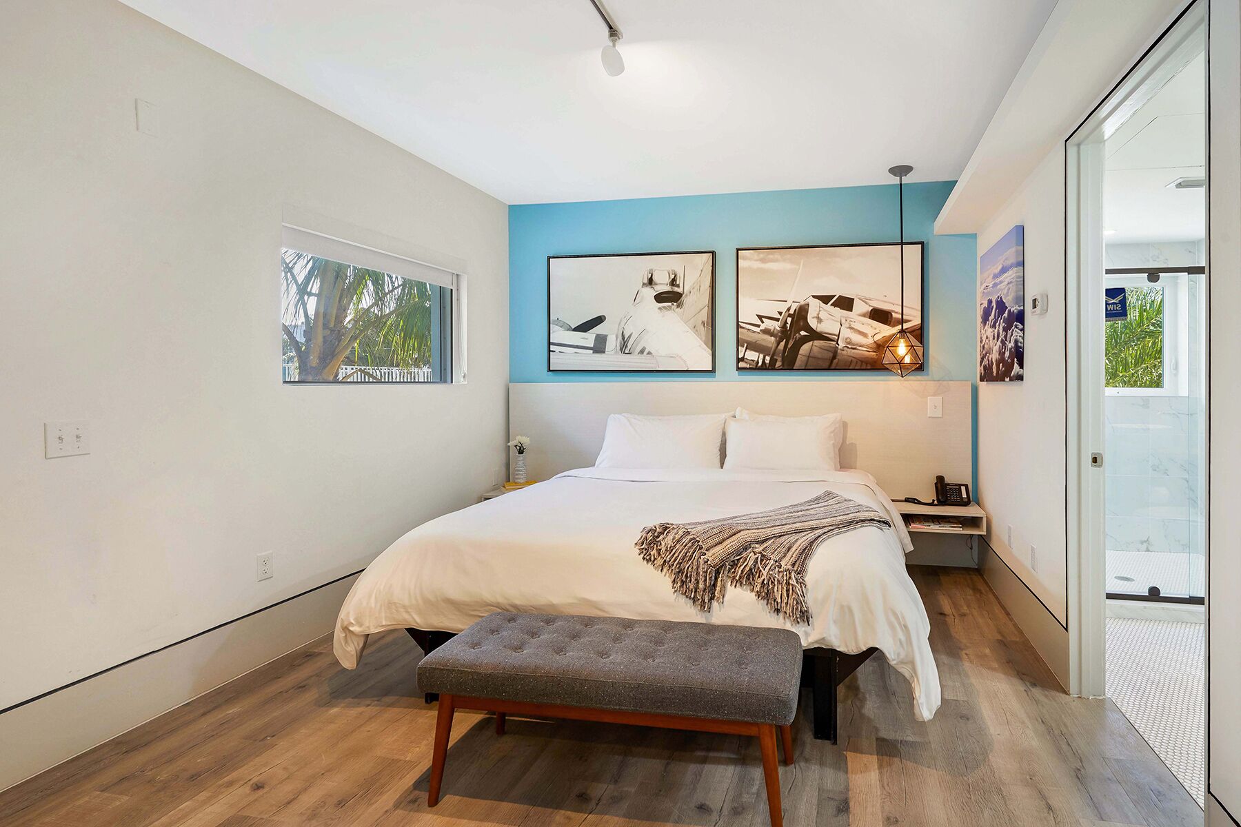 A modern bedroom with a large bed, a bench, and artwork on the walls.