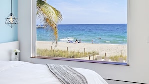 A bedroom with a large window overlooking a beach. - Ocean Treasure Beachside Suites (Lauderdale-by-the-Sea)