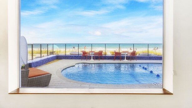 A pool area with a view of the beach, a covered seating area, and a fenced deck. - Ocean Treasure Beachside Suites (Lauderdale-by-the-Sea)