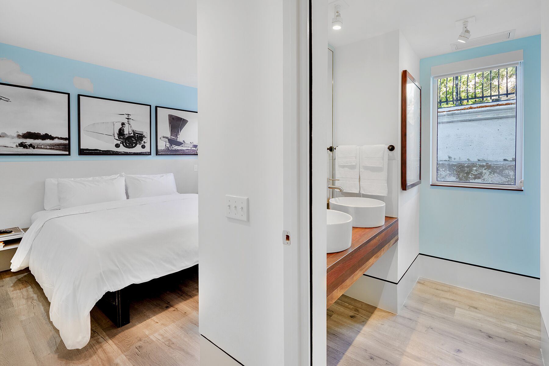 A modern bedroom with a bed, a bathroom with a sink and mirror, and a view of the sea through a window.