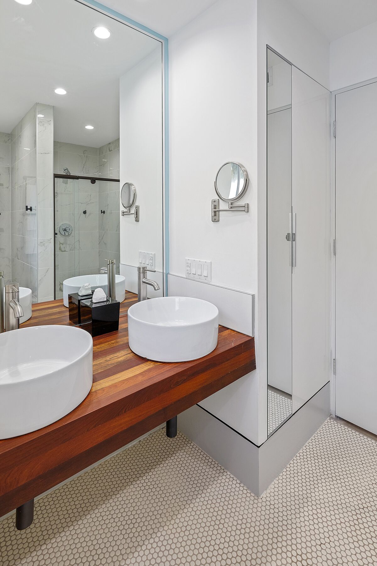 A modern bathroom with two large white sinks, a wooden vanity, a glass shower enclosure, and a large mirror.