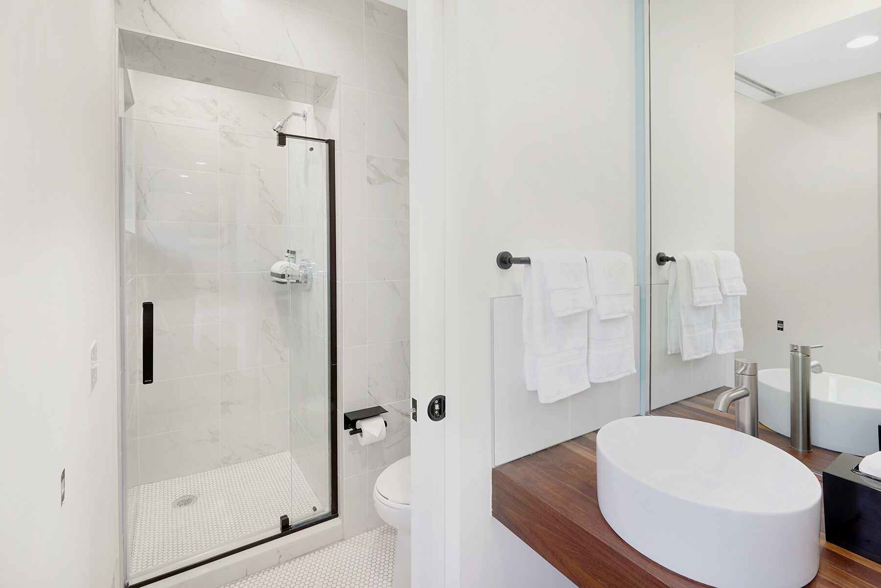 A modern bathroom with a glass-enclosed shower, a wooden vanity with a white sink, and a large mirror.