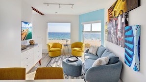 A modern living room with a view of the beach, featuring a sofa, yellow chairs, and artwork on the walls. - Ocean Treasure Beachside Suites (Lauderdale-by-the-Sea)
