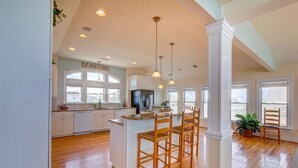 A spacious kitchen with wooden flooring, white cabinetry, and a central island with bar stools. - 2869 - Seascape - Oceanfront Duck Retreat w/ Pool, Hot Tub & Views (Kitty Hawk)