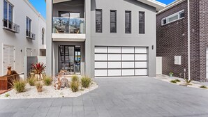 A modern two-story house with a garage, a balcony, and a landscaped front yard. - Maggie's Place Beachfront Retreat in Corlette (Corlette)