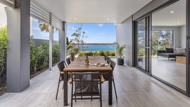 A modern outdoor dining area with a view of the sea, a wooden table, and black chairs. - Maggie's Place Beachfront Retreat in Corlette (Corlette)