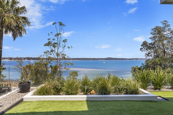 A coastal landscape with a clear view of the sea, a sandy beach, and a variety of vegetation including palm trees and shrubs. - Maggie's Place Beachfront Retreat in Corlette (Corlette)