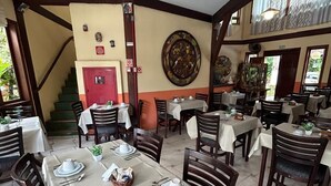 A restaurant with multiple tables set for dining, a staircase, and a large decorative wall piece. - Recanto Verde Praia Hotel (São Sebastião)