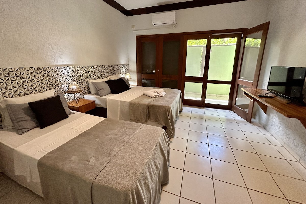 A hotel room with two beds, a TV, and a sliding glass door leading to an outdoor area.