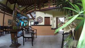 A reception area with a wooden reception desk, chairs, a decorative wall with a clock, and a large potted plant. - Recanto Verde Praia Hotel (São Sebastião)