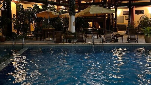 A pool area with lounge chairs and umbrellas, surrounded by a multi-story building with wooden balconies and warm lighting. - Recanto Verde Praia Hotel (São Sebastião)