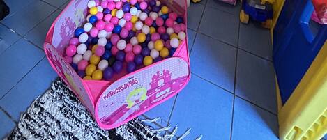 Zona infantil con piscina de pelotas, juguetes y una ventana con cortinas.