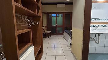 A hallway with a wooden wardrobe, a tiled floor, and a view into a room with a sink and a chair.