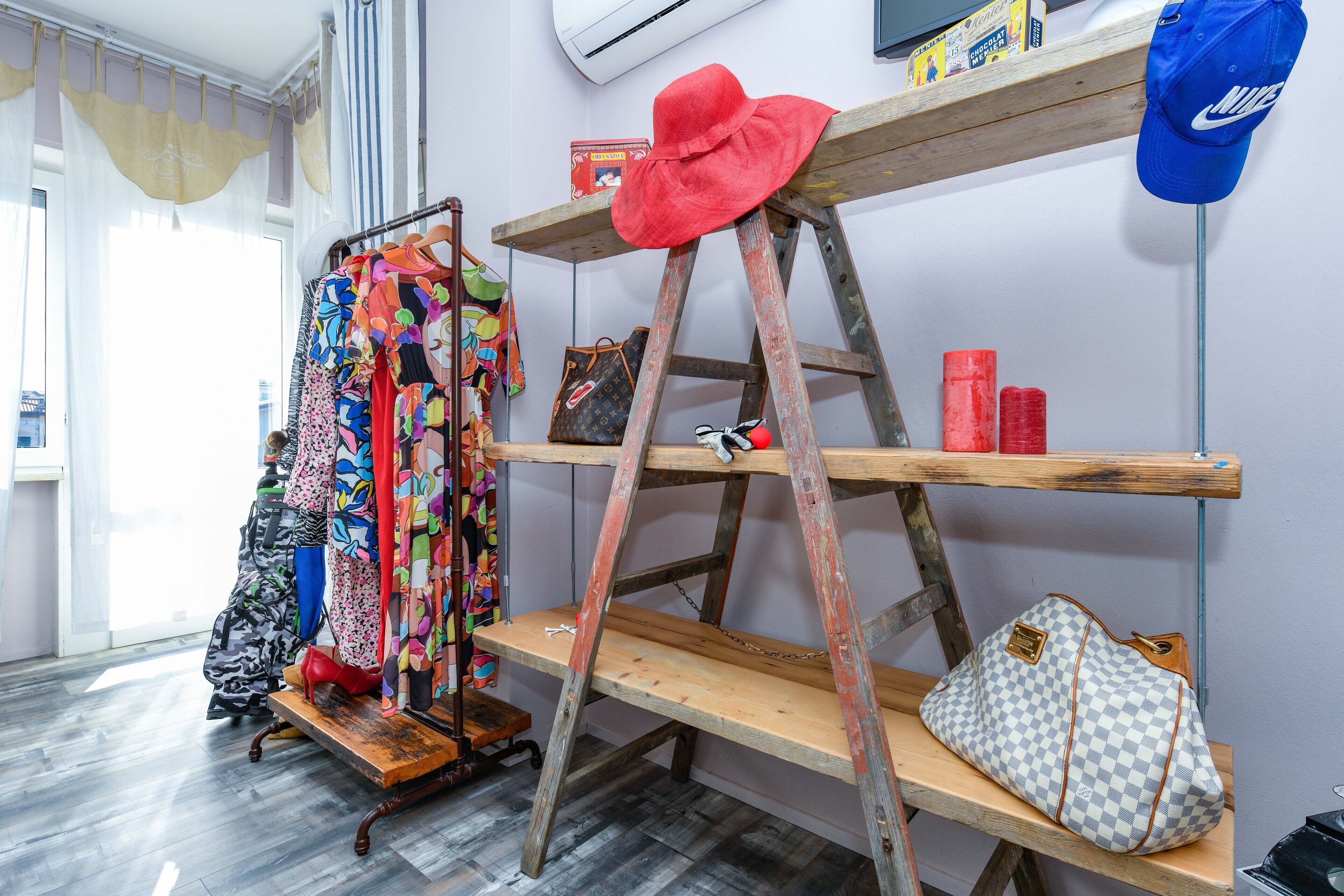 A room with a wooden ladder shelf, a clothing rack, and a shoe rack.