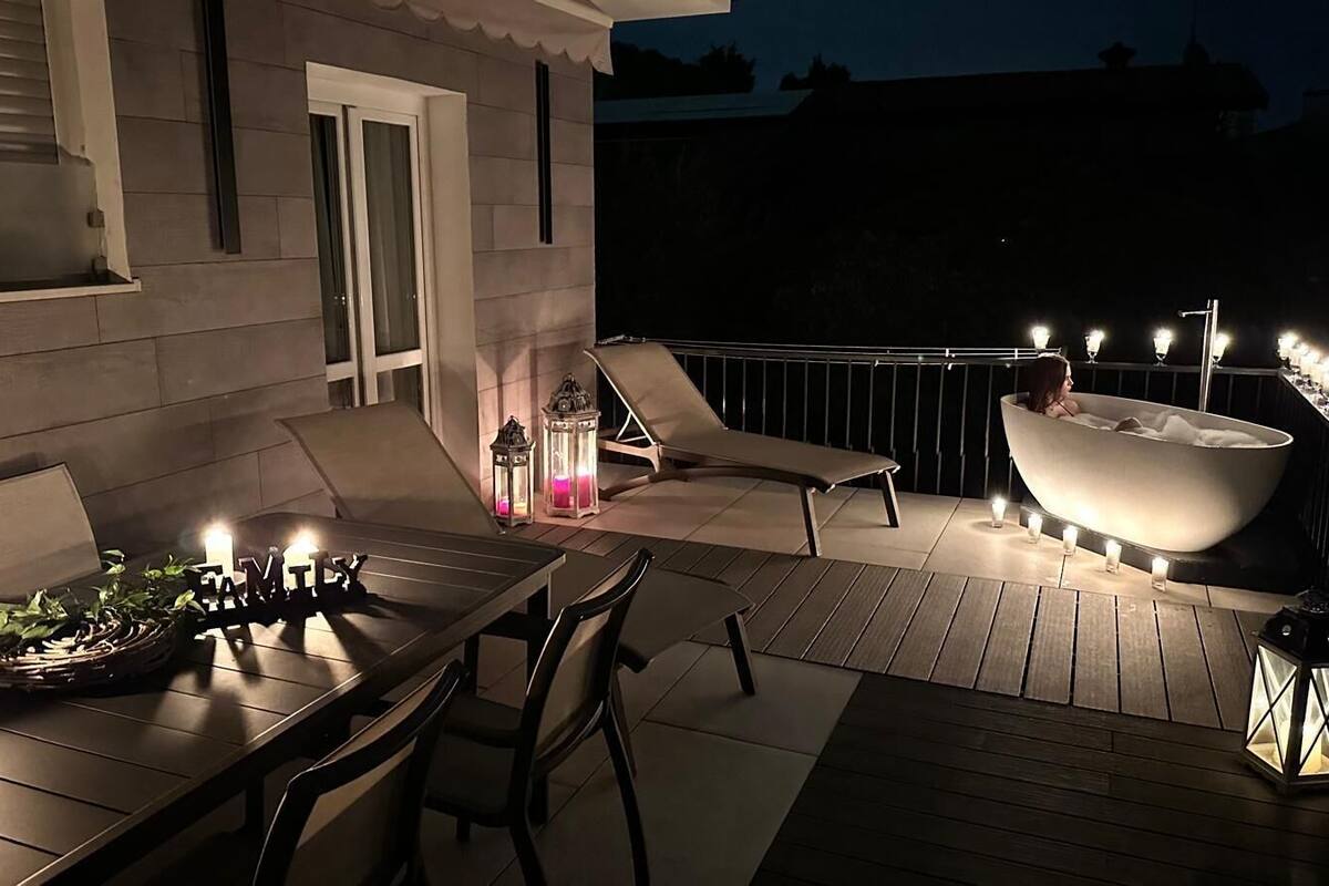 An outdoor patio with a dining table, chairs, a lounge chair, a hot tub, and candles.