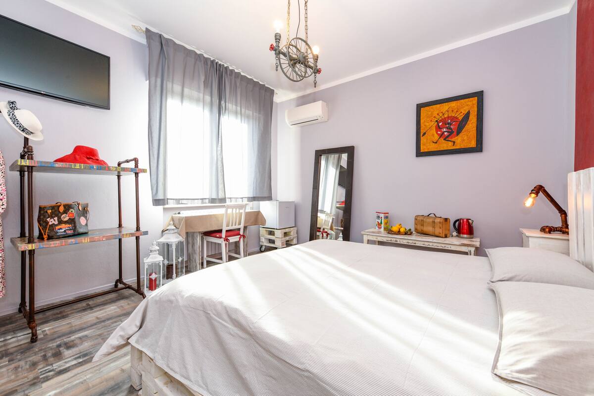 A bedroom with a bed, desk, chair, and a TV on the wall.