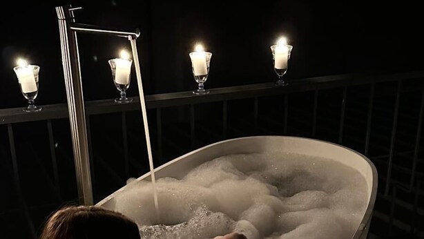 Eine Person entspannt sich in einer Badewanne, umgeben von Kerzen.