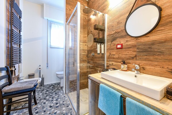Un baño moderno con pared de madera, un espejo grande, ducha e lavamanos.