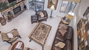Ein geräumiges Wohnzimmer mit Kamin aus Stein, Ledersofas, einem Couchtisch und einem Deckenventilator.