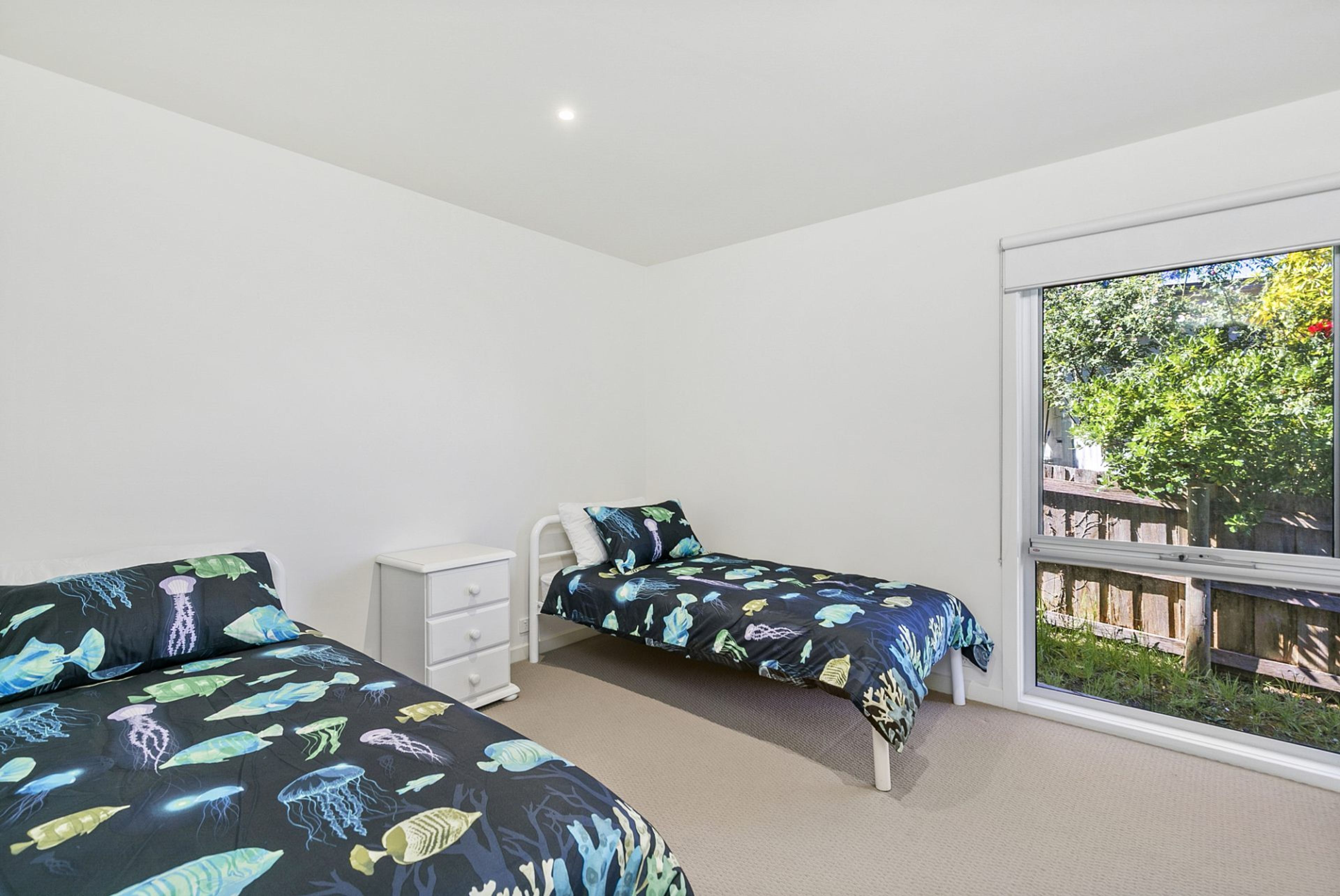 A bedroom with two beds, a white dresser, and a large window with a view of greenery.