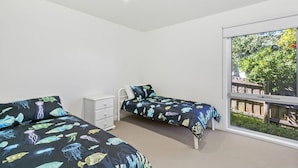 A bedroom with two beds, a white dresser, and a large window with a view of greenery.