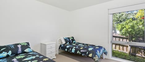 Une chambre avec deux lits, une commode blanche et une grande fenêtre donnant sur un paysage verdoyant.