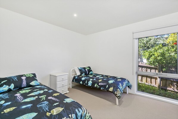 A bedroom with two beds, a white dresser, and a large window with a view of greenery.