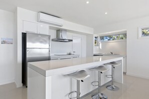 A modern kitchen with a stainless steel refrigerator, a built-in oven, a range hood, and a large island with bar stools.
