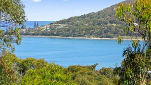 A coastal landscape with a clear view of the sea, a hill with dense vegetation, and a cluster of buildings in the background.